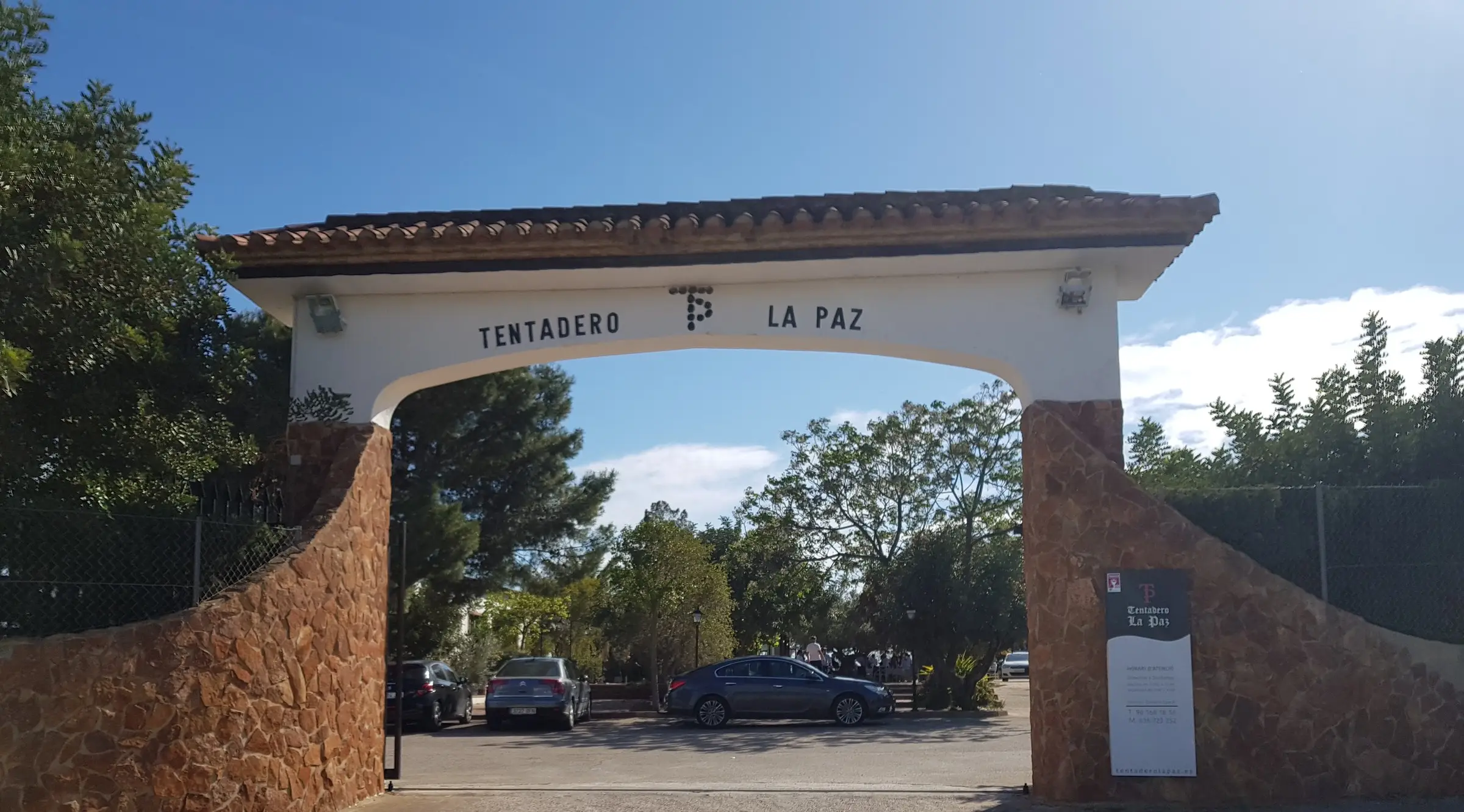 El arco de entrada a la finca, con el rótulo «Tentadero La Paz», entre pinos y bajo un cielo azul