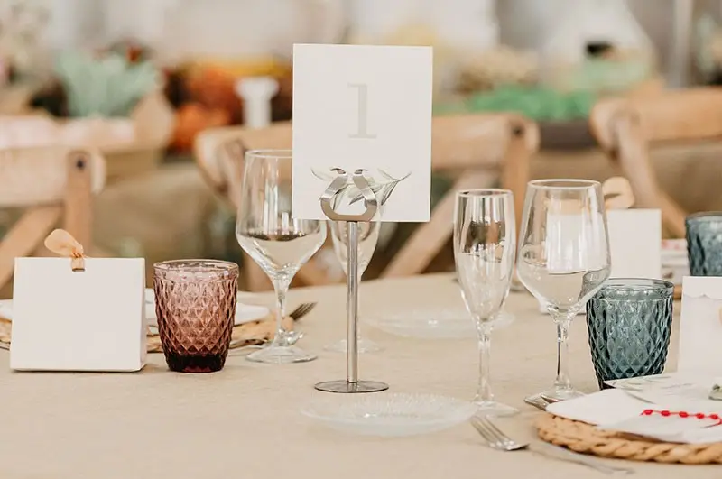 Detalle de una mesa: el número 1, copas y vasos de cristal de colores