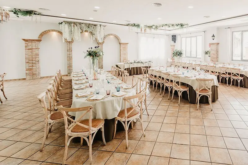 Salón con arcos blancos, suelo de barro y mesas imperiales vestidas de blanco