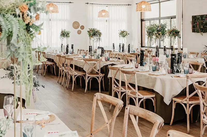 Salón de suelo de madera con mesas redondas e imperiales, flores y lámparas de fibra